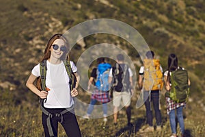 Young girl tourist in glasses with a backpack on a hiking trip in the mountains on a hill in summer nature.