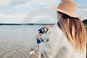 Young girl tourist pours hot tea out of thermos by autumn lake enjoying landscape. Travelling