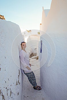 A young girl tourist in white clothes smiles and fills on the white walls of the city of Fira.