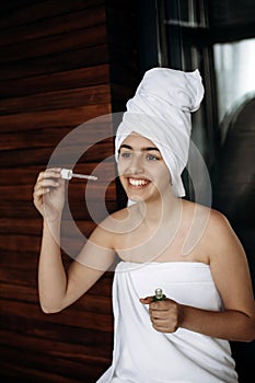 Young girl with towel on her head makes facial treatments. Skin care, moisturizing with serum