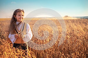 Young girl in traditional Bulgarian folklore costume at the agricultural wheat field during harvest time with industrial combine