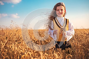 Young girl with traditional Bulgarian folklore costume at the agricultural wheat field during harvest time with industrial combine