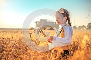 Young girl with traditional Bulgarian folklore costume at the agricultural wheat field during harvest time with industrial combine