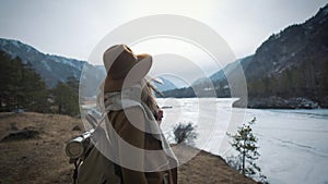 A young girl traveler approaches the edge of the cliff shore. He looks out into the distance to the frozen river in