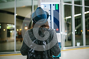 Young girl traveler with a backpack in a hat looks at the information board at the airport. Getting information about