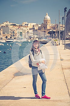 Young girl traveler stay and posing on embankment of Kalkara Creek of Malta's Grand Harbour