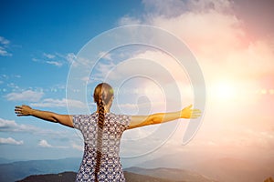 Young girl traveller raised her arms on background of sunset in mountains