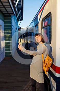 young girl travels. beautiful tourist takes a selfie at the station near the train. Girl with a backpack
