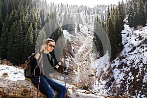 Young girl with trekking sticks resting on a fallen tree in the background of snow-capped mountains