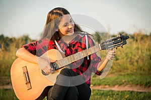 Young girl tunes the guitar on meadow at sunset