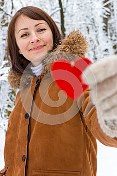 Young girl with unfocused red wooden heart in winter forest. Valentines day and Christmas holidays. Winter concept.