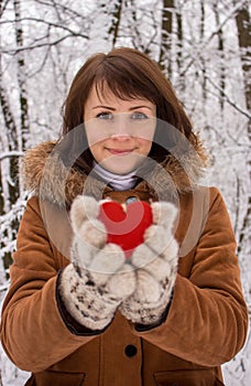 Young girl with unfocused red wooden heart in winter forest. Valentines day and Christmas holidays. Winter concept.