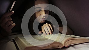 Young girl using flashlight in dark for reading book under the blanket