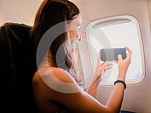 young girl using smartphone and looking through the window on airplane