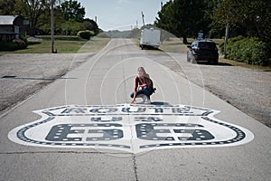 A young girl on vacation crouched in front of the US Route 66 traffic sign