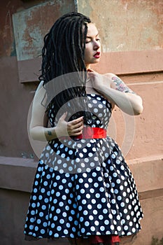 Young girl in vintage black dress in white peas with black dreadlocks on head and red lipstick on lips