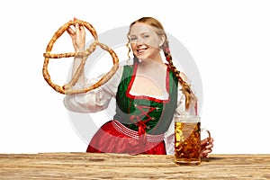 Young girl waitress, wearing a traditional Bavarian or German dirndl, serving big beer mugs with huge pretzel