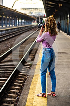 Young girl walking alone on train platform and taking photos on railway station