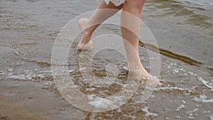 Young girl walking along sand shore or Beach. Close Up.Legs Of Girl Stepping And Relaxing On Sandy Coast. Hot Summer Day