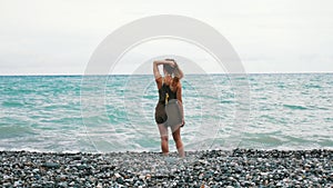 Young girl walking along the sea rocky coast. There are waves. The girl`s long hair is blown up by the wind.