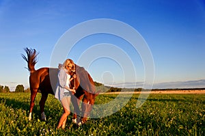 Young girl walking with a horse in the field