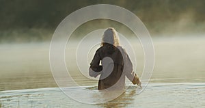 Young girl walking in the lake with a box and she is dragging a knife by her side, In the natural green view, slow