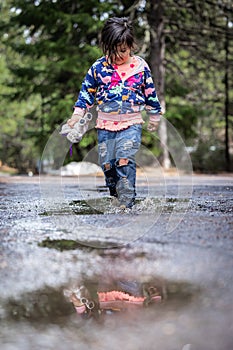 A young girl is walking through a puddle of water, holding a toy in her hand