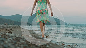 Young girl walking at sea beach at sunset. Girl in dress walk on seaside