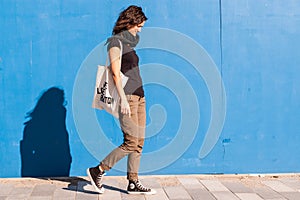 Young girl walking on street with blue wall in background.