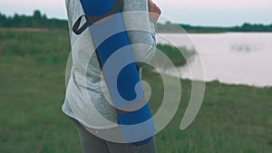 Young girl walking to do yoga practice at coast. Woman holding blue yoga mat