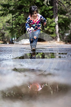 A young girl is walking on a wet road, with her reflection in the water