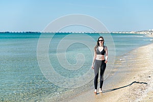 A young girl walks along the beach after a run in sunglasses