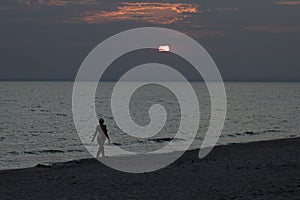 A young girl walks along an empty beach, walks along the coastline at sunset