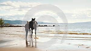 A young girl walks on the beach with a horse