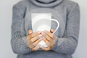 A young girl in a warm gray sweater holding a large white cup. Conceptually for the winter holidays. Winter mood.