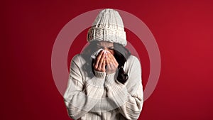 Young girl in warm knitted wear sneezes into tissue. Isolated woman is sick