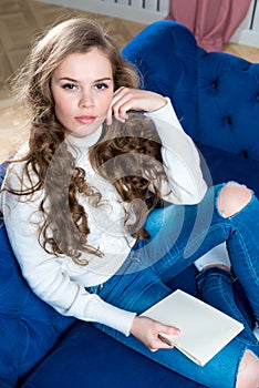 young girl in a warm sweater and jeans on the couch with a notebook