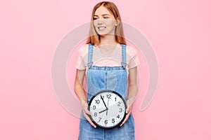 Young girl with a watch in her hands, on an isolated pink background