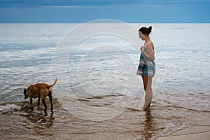 Young girl watching dog drinking water by the sea