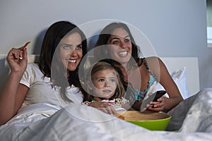 Young girl watching TV in bed with gay female parents