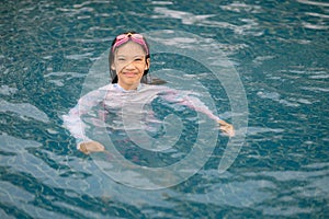 A young girl is in the water wearing a white shirt and pink goggles