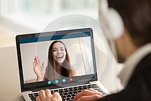 Young girl waving from laptop screen at man in headphones.