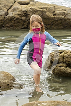 Young girl wearing a mask and colorful swimming suit having fun splashing at the beach