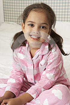 Young Girl Wearing Pajamas Sitting On Bed