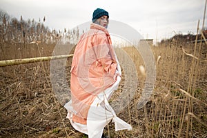 A young girl wearing a pastel coat and a stylish hat poses in a wheat field. Back viev