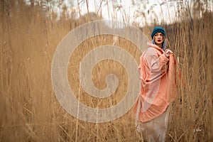 A young girl wearing a pastel coat and a stylish hat poses in a wheat field. Back viev