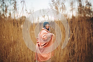 A young girl wearing a pastel coat and a stylish hat poses in a wheat field. Back viev