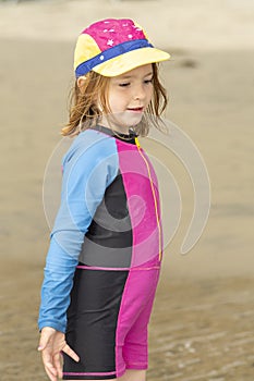 Young girl in a hat and colorful swimming suit having fun splashing at the beach