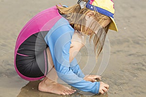 Young girl in a hat and colorful swimming suit having fun splashing at the beach