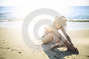 Young girl wearing red bikini sitting on the beach.